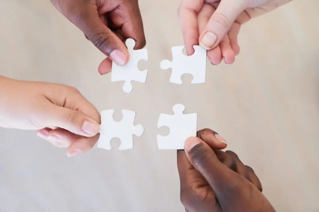 Four different hands each holding a white puzzle piece that are able to connect together