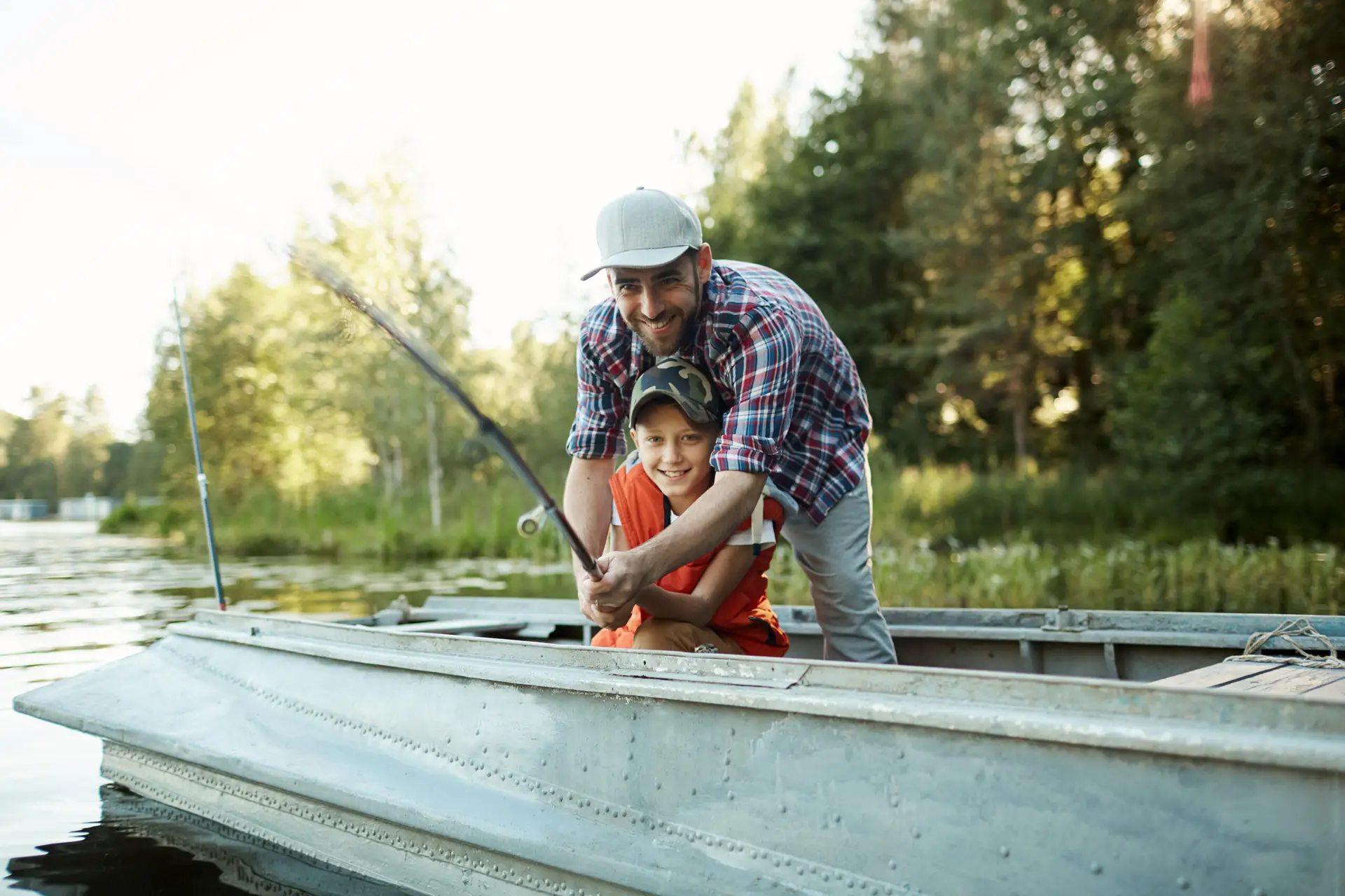 Father and son holding rod while sitting in boat and fishing