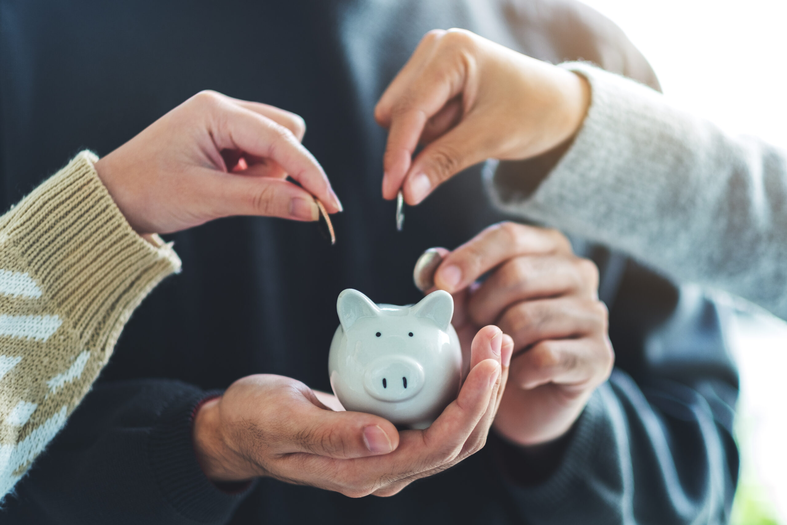 Close-up image of people holding and putting coins into piggy bank