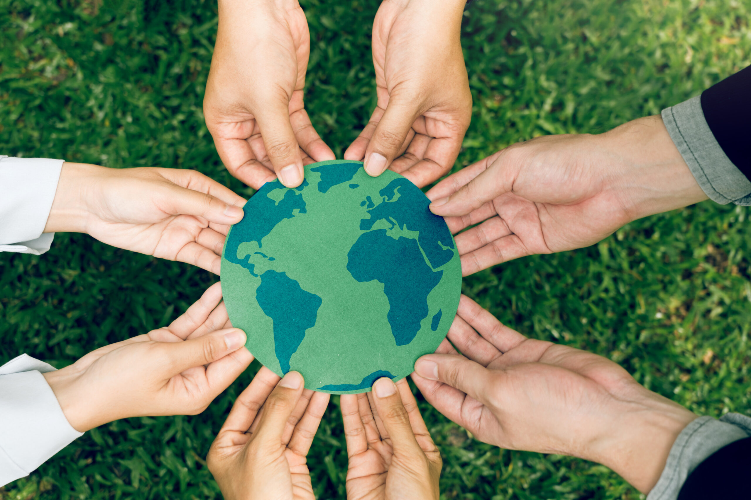 Multiple hands holding a flat cutout of the Earth.