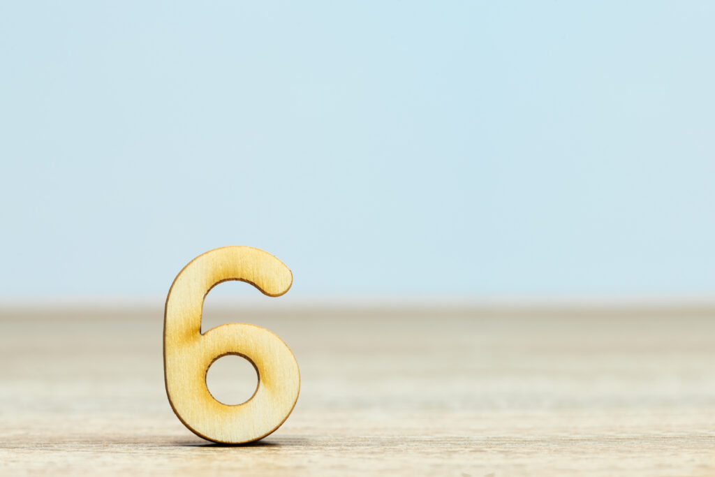 Wooden number six sitting up on a table with light blue background
