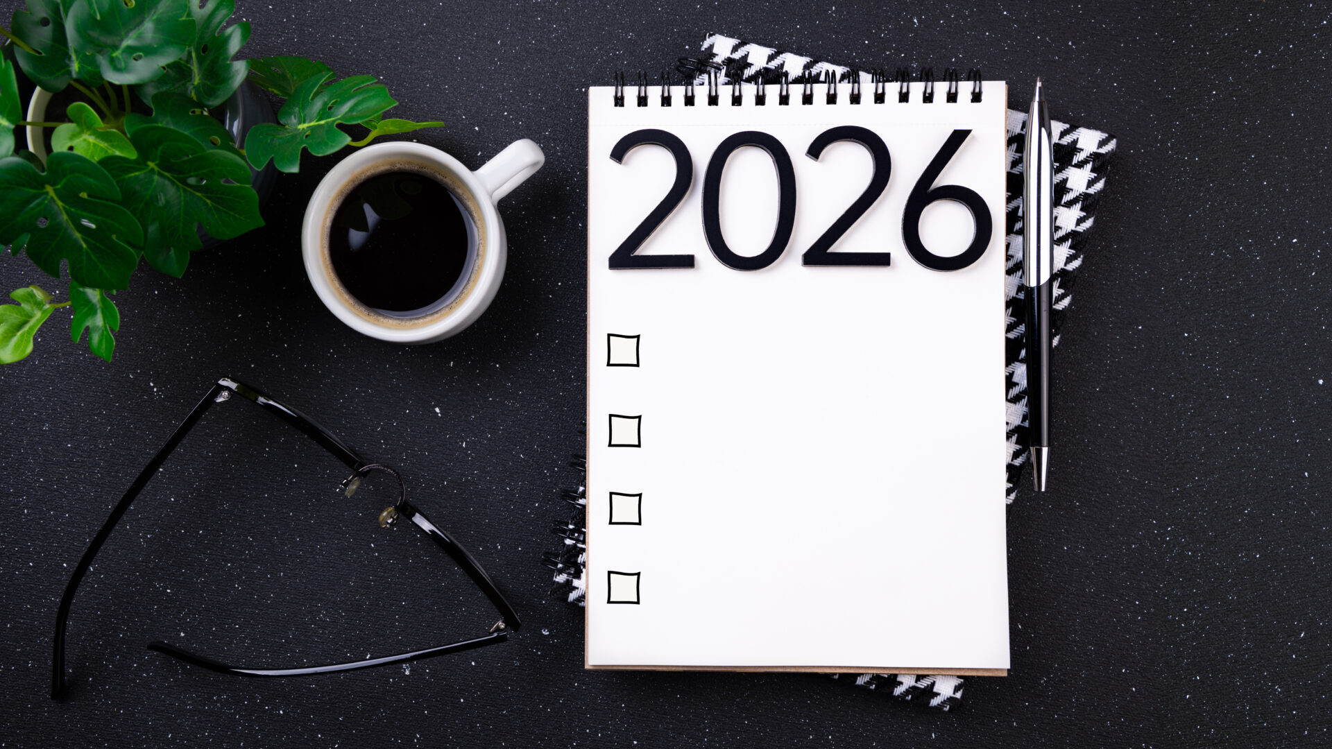 2026 goals list with notebook, coffee cup, plant on black table.